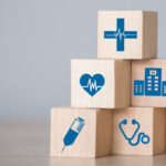 Stacked wooden blocks with blue health symbols including a heart rate, vaccine, wheelchair, hospital